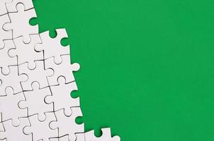 Fragment of a folded white jigsaw puzzle on the background of a green plastic surface. Texture photo with copy space for text