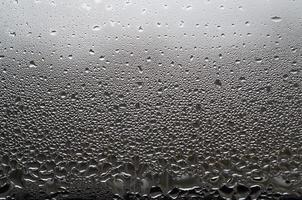 A photo of the glass surface of the window, covered with a multitude of droplets of various sizes. Background texture of a dense layer of condensate on glass