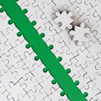 The green path is laid on the platform of a white folded jigsaw puzzle. The missing elements of the puzzle are stacked nearby. Texture image with space for text photo