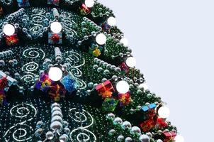 A fragment of a huge Christmas tree with many ornaments, gift boxes and luminous lamps. Photo of a decorated Christmas tree close-up with copy space