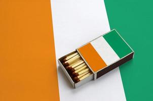 Ivory Coast flag is shown in an open matchbox, which is filled with matches and lies on a large flag photo
