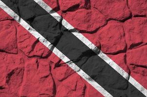 Trinidad and Tobago flag depicted in paint colors on old stone wall closeup. Textured banner on rock wall background photo