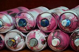 Still life with a large number of used colorful spray cans of aerosol paint lying on the treated wooden surface in the artist's graffiti workshop. Dirty and stained cans for spray art photo