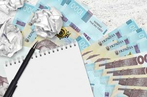 1000 Ukrainian hryvnias bills and balls of crumpled paper with blank notepad. Bad ideas or less of inspiration concept. Searching ideas for investment photo