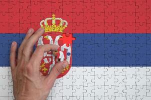 Serbia flag is depicted on a puzzle, which the man's hand completes to fold photo