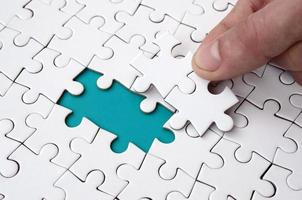 The human hand fills the last missing elements of the surface from the jigsaw puzzle. The concept of the completion of the initiated cases photo