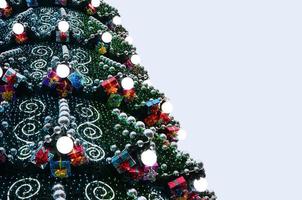 un fragmento de un enorme árbol de navidad con muchos adornos, cajas de regalo y lámparas luminosas. foto de un primer plano de árbol de Navidad decorado con espacio de copia