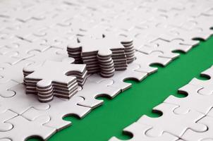 The green path is laid on the platform of a white folded jigsaw puzzle. The missing elements of the puzzle are stacked nearby. Texture image with space for text photo