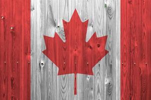 Canada flag depicted in bright paint colors on old wooden wall. Textured banner on rough background photo