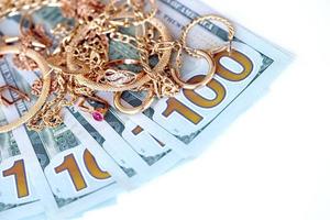 muchos costosos anillos, aretes y collares de joyería dorada con una gran cantidad de billetes de dólares estadounidenses sobre fondo blanco. casa de empeño o joyería foto