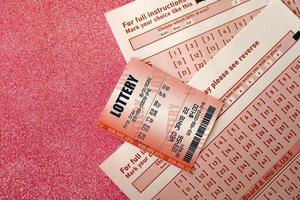 Red lottery ticket lies on pink gambling sheets with numbers for marking to play lottery. Lottery playing concept or gambling addiction. Close up photo