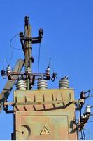 Old and obsolete electrical transformer against the background of a cloudless blue sky. Device for distribution of supply of high-voltage energy photo