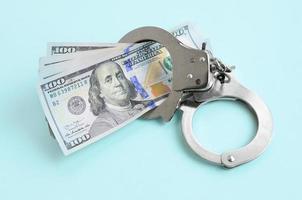 Silver police handcuffs and hundred dollar bills lies on light blue background photo