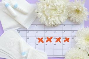 almohadillas menstruales y tampones en el calendario del período de menstruación con flores blancas sobre fondo lila foto