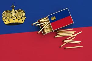 Liechtenstein flag is shown on an open matchbox, from which several matches fall and lies on a large flag photo