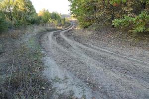 Autumn landscape with a curved road and traces of the tread of large wheels of agricultural machinery photo