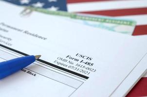 I-485 Application to register permanent residence or adjust status form and green card from dv-lottery lies on United States flag with blue pen from Department of Homeland Security photo