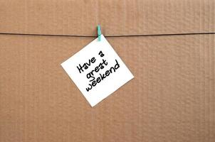 Have a great weekend. Note is written on a white sticker that hangs with a clothespin on a rope on a background of brown cardboard photo