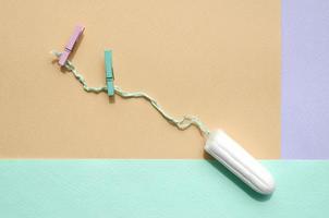 Tampon with two clothespins lie on texture background of fashion pastel violet, yellow and blue colors photo