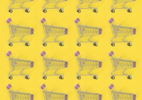 Shopping addiction, shopping lover or shopaholic concept. Many small empty shopping carts perform a pattern on a pastel colored paper background. Flat lay composition, top view photo