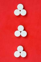varias tabletas blancas yacen sobre un fondo rojo brillante en forma de tres flechas triangulares. imagen de fondo sobre medicina y temas farmacéuticos foto