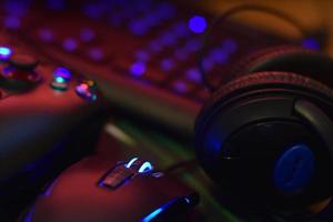 Modern gamepad and gaming mouse lies with keyboard and headphones on table in dark playroom scene. Video game challenges and competitions concept photo