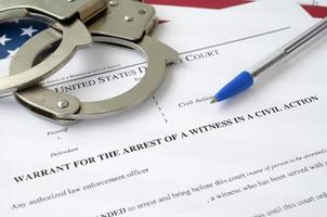 District court warrant for the arrest of a witness in a civil action papers with handcuffs and blue pen on United States flag. Permission to witness arrest photo