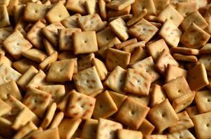 A lot of small cookies are square shaped. A pattern of a yellow salt cracker. Background image with salted pastry photo