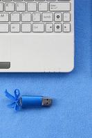 la tarjeta de memoria flash usb azul brillante con un lazo azul se encuentra sobre una manta de tela polar azul claro suave y peluda junto a una computadora portátil blanca. diseño clásico de regalo femenino para una tarjeta de memoria foto