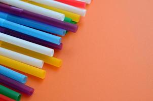 Many colorful straws for drinks lies on a bright orange background surface photo