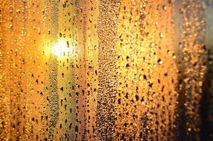 The texture of misted glass with a lot of drops and drips of condensation against the sunlight at dawn. Background image photo