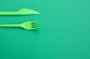 Disposable plastic cutlery green. Plastic fork and knife lie on a green background surface photo