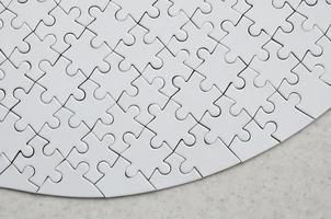 A white jigsaw puzzle in the complete form lies on a treated stone surface. Textured image with copy space photo