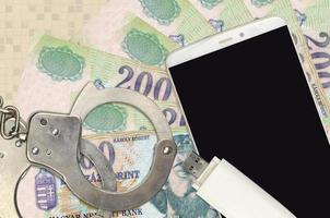 200 Hungarian forint bills and smartphone with police handcuffs. Concept of hackers phishing attacks, illegal scam or malware soft distribution photo
