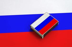 Russia flag is pictured on a matchbox that lies on a large flag photo