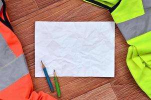 A crumpled sheet of paper with two pencils surrounded by green and orange working uniforms photo