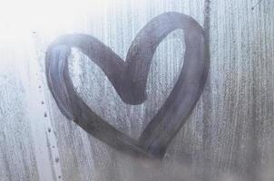 A heart-shaped drawing drawn by a finger on a misted glass in rainy weather photo