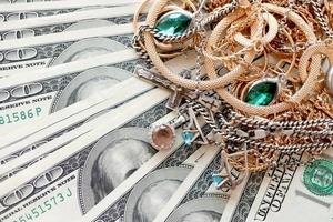 Many expensive golden and silver jewerly rings, earrings and necklaces on big amount of US dollar bills close up. Pawnshop or jewerly shop photo