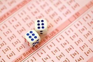 Dice cubes lies on pink gambling sheets with numbers for marking to play lottery. Lottery playing concept or gambling addiction. Close up photo