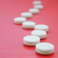 A few white tablets lie on a bright red background surface. Background image on medical and pharmaceutical topics photo