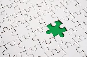 Close-up texture of a white jigsaw puzzle in assembled state with missing elements forming a green pad for text. Copy space photo