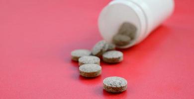 Several brown tablets fall out of the plastic jar on the red surface. Background image on medical and pharmaceutical topics photo