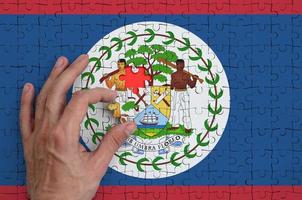 Belize flag is depicted on a puzzle, which the man's hand completes to fold photo