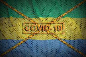 Gabon flag and Covid-19 stamp with orange quarantine border tape cross. Coronavirus or 2019-nCov virus concept photo