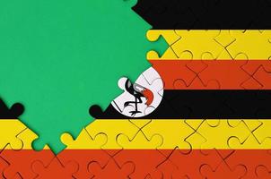 Uganda flag is depicted on a completed jigsaw puzzle with free green copy space on the left side photo