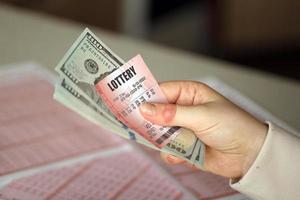 una mujer joven sostiene el billete de lotería con una fila completa de números y billetes de dólar en el fondo de las hojas en blanco de la lotería foto