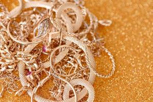 Many expensive golden jewerly rings, earrings and necklaces on golden glitter background with shiny sparkles. Pawn shop or jewerly trading photo