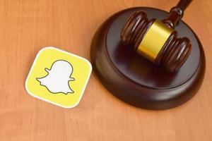 KHARKOV, UKRAINE - MAY 3, 2022 Snapchat paper logo lies with wooden judge gavel. Entertainment lawsuit concept photo