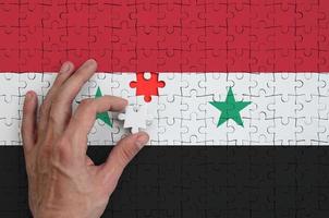 Syria flag is depicted on a puzzle, which the man's hand completes to fold photo