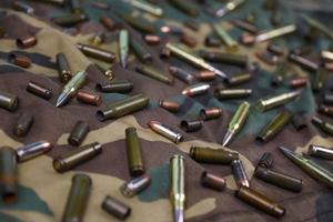 Many rifle bullets and cartridges on dark camouflage background photo